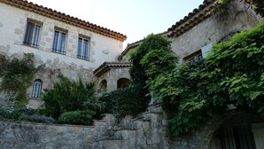 Un bâtiment en pierre doté de fenêtres en arc de cercle et d’un toit recouvert de tuiles, entouré d’une végétation luxuriante.