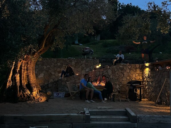 Un espace de détente avec des sièges en pierre et un foyer, entouré d’arbres et agrémenté d’un banc en pierre.