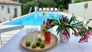 Une table placée au bord de la piscine, avec des verres, des citrons verts, une bouteille de Schweppes et une plante en pot.
