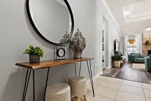 A modern interior with a wooden console table, a round mirror, a clock, and two woven stools.