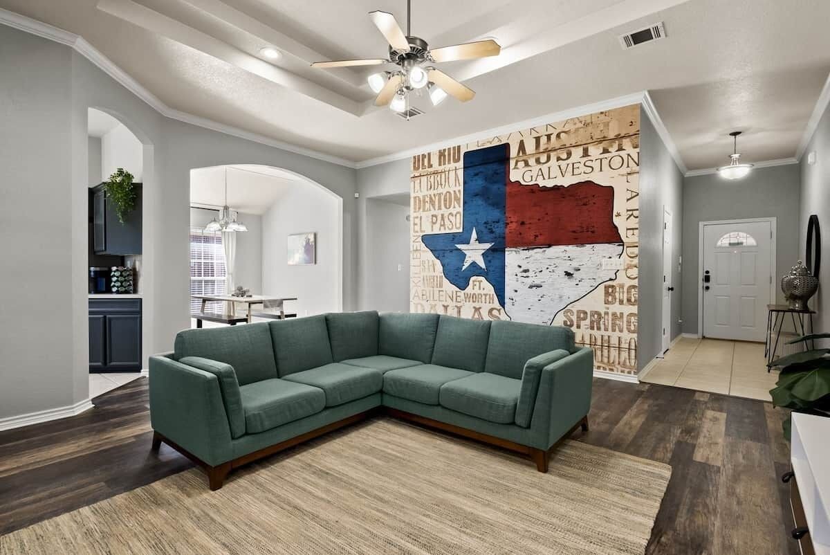 A modern living room with a sectional sofa, a ceiling fan, and a wall mural.