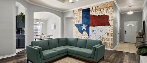 A modern living room with a sectional sofa, a ceiling fan, and a wall mural.