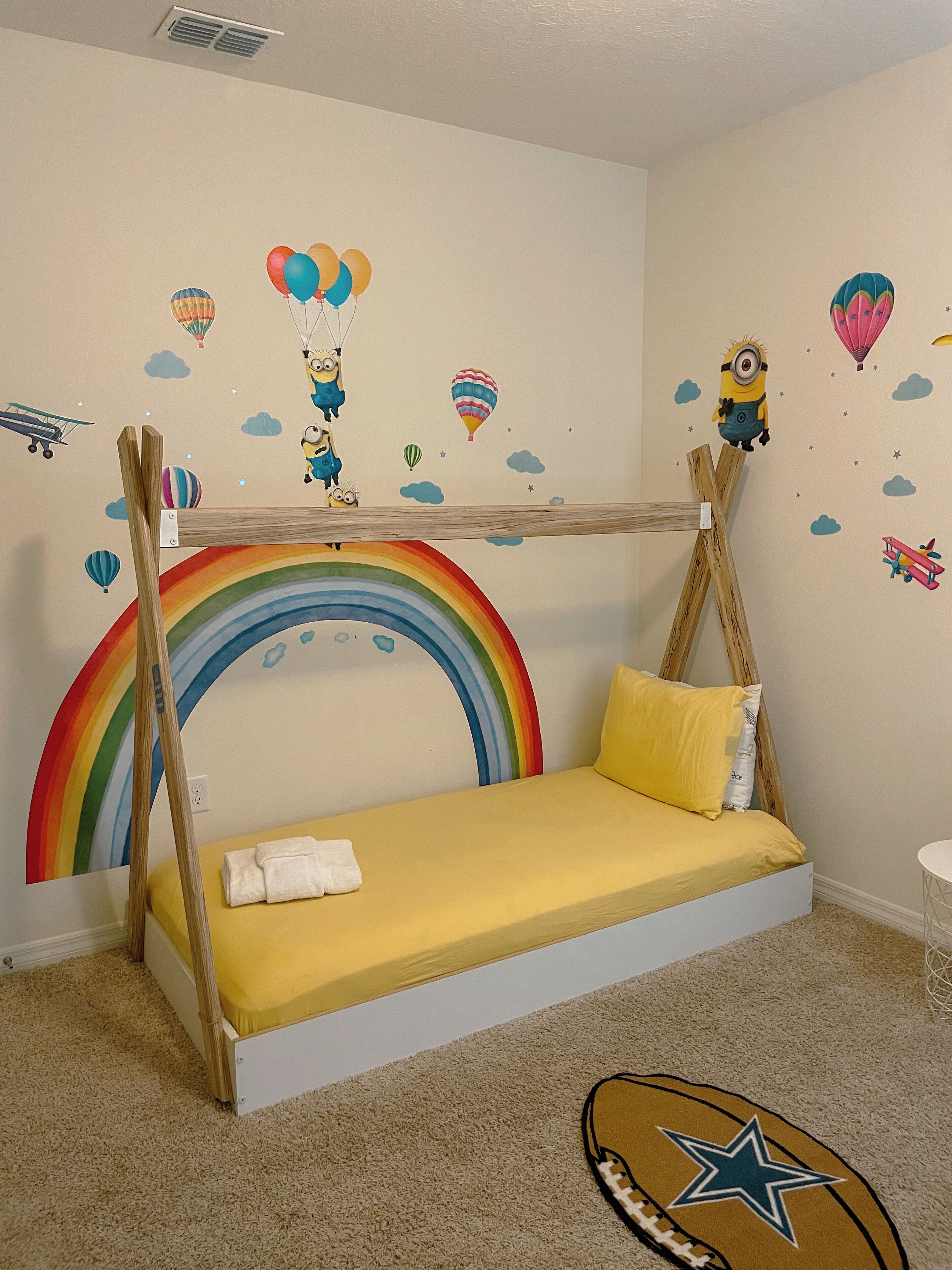 A child’s bedroom with a bunk bed, a rainbow wall decal, and a Minion-themed wall.