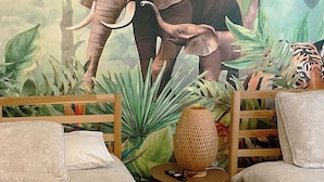 Ein Zimmer mit Wandgemälde eines Elefanten, einem Bett, einem Sessel und einem kleinen Tisch mit Lampe.