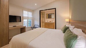 A hotel room with a bed, a TV on a wooden desk, a bathroom with a mirror, and a window with blinds. - 1 Bedroom : Scandinavian Urban 4 in city center (Cannes)