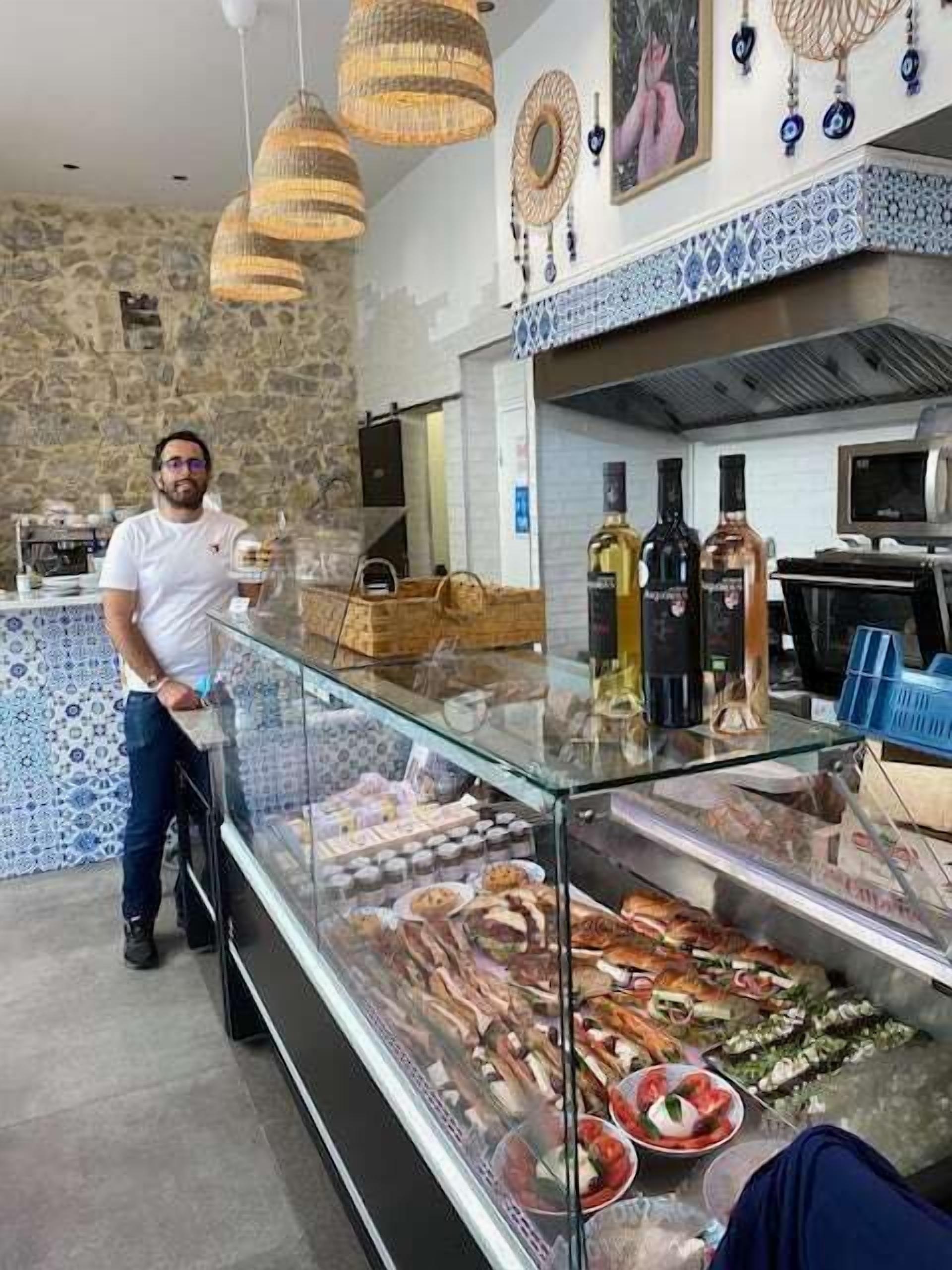 Un comptoir de charcuterie proposant diverses sortes de viandes et de fromages, une personne derrière le comptoir, et des éléments décoratifs sur les murs.