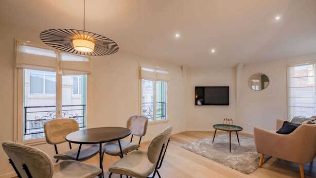 A modern living room with a round table, four chairs, a sofa, a TV mounted on the wall, and large windows with balconies. - 1 Bedroom : Scandinavian Urban 4 in city center (Cannes)