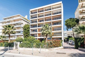 A multi-story building with balconies, a gated entrance, and surrounding greenery.