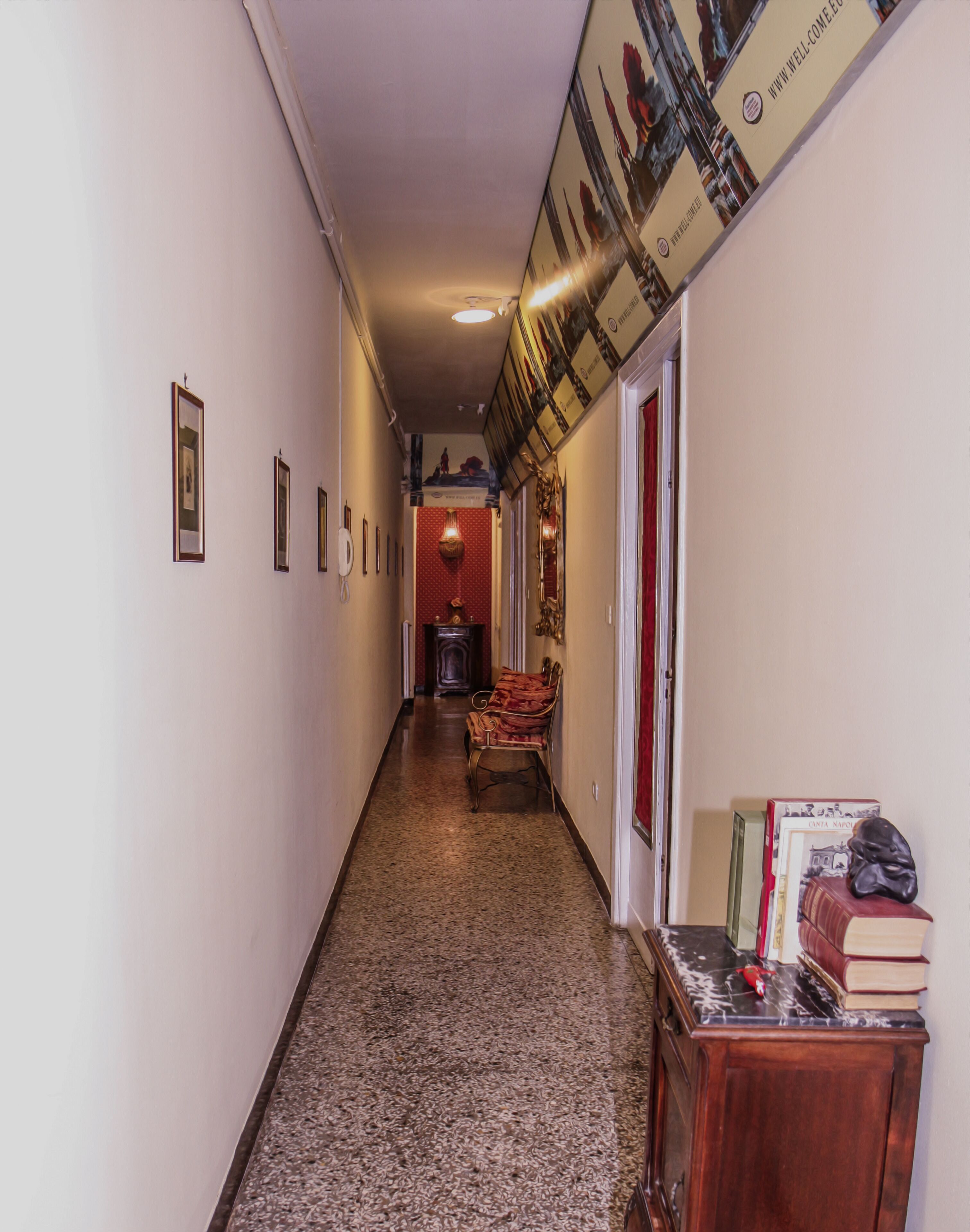 Un pasillo con cuadros enmarcados en las paredes, un banco y una pequeña mesa con libros y un busto.