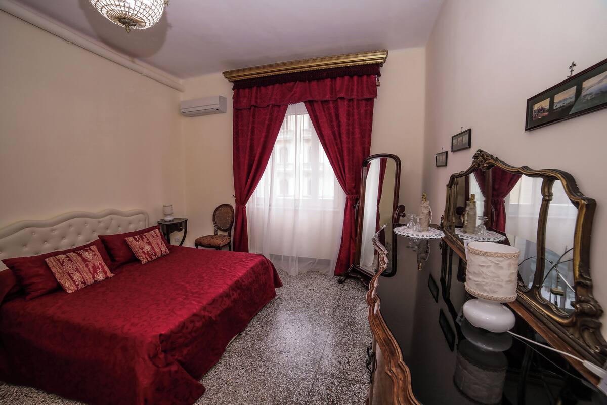 A bedroom with a large bed, a vanity with a mirror, and a window with red curtains.