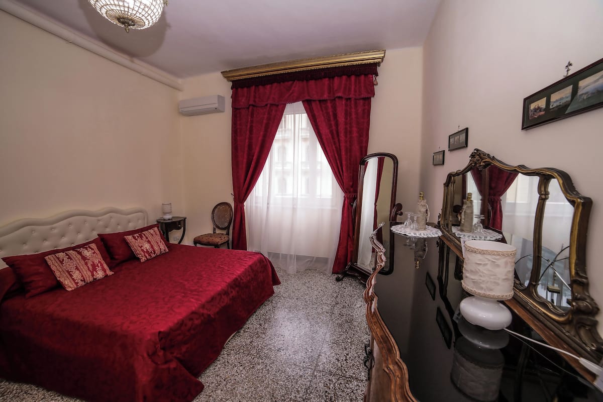 A bedroom with a large bed, a vanity with a mirror, and a window with red curtains.