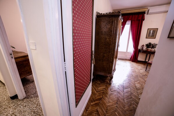 A hallway with a wooden herringbone floor, a red patterned door, and a wooden cabinet. - WELL COME - SANTA LUCIA (Naples)