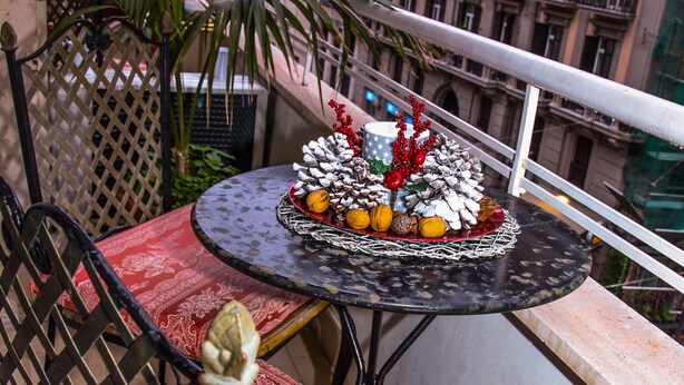 Un balcon avec une table ronde, une nappe rouge à motifs, un élément décoratif en guise de centre de table et une chaise avec un dossier ajouré.