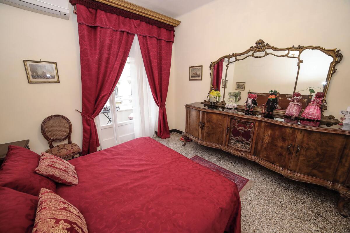 A bedroom with a large bed, a wooden dresser with a mirror, and red curtains.