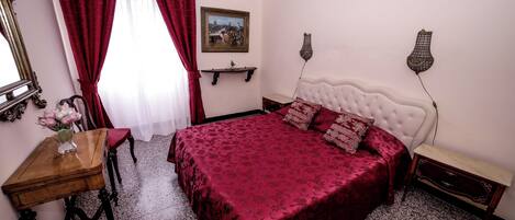 Un dormitorio con una cama, un escritorio, una silla, un jarrón de flores y un cuadro en la pared.