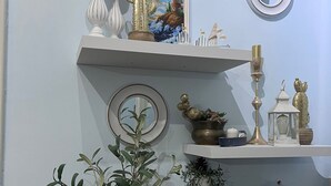 Une pièce avec un radiateur blanc, une plante en pot, un tableau encadré et divers objets décoratifs disposés sur des étagères.