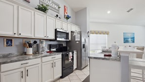 A modern kitchen with white cabinets, a stainless steel refrigerator, a microwave, and a stove. There is a small island with a sink and a countertop. - 'Disney Dreams' Spacious 4 Bed home with Private pool & Spa (Clermont)