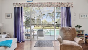 A living room with a sofa, armchair, and a view of a swimming pool through glass doors. - 'Disney Dreams' Spacious 4 Bed home with Private pool & Spa (Clermont)