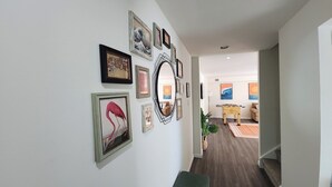 A hallway with framed artwork on the walls, a bench, and a foosball table in the background.