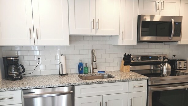 A modern kitchen with white cabinets, stainless steel appliances, a coffee maker, and a kettle on the countertop.