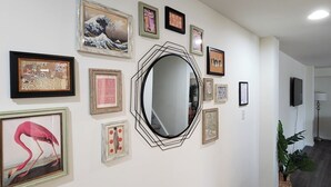 A hallway with various framed artworks on the walls, a large mirror, and a potted plant.
