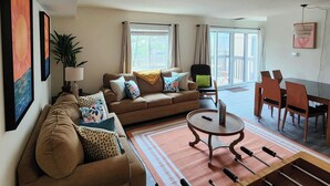 A living room with a sofa, coffee table, and dining area with chairs.