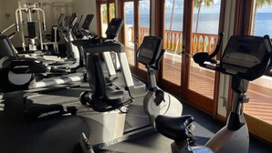 Un gimnasio con numerosas cintas de correr y equipo de ejercicio, amplias ventanas con vista al océano.