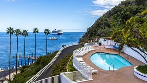 Zona de piscina con sillones de descanso, una piscina y vista al océano con un crucero a lo lejos.