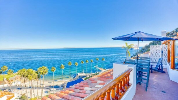 Un balcón con vistas al océano, una sombrilla azul y una zona de piscina con sillones de relax.