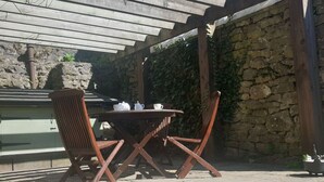 Una terrazza esterna con tavolo e sedie in legno, un muro in pietra e un pergolato sovrastante.