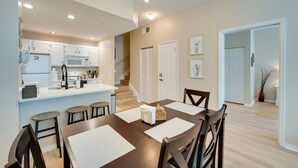 A modern kitchen with white cabinets, a central island, and a dining area with a dark wooden table and chairs. - Family Escape Near Disney | Resort Amenities (Kissimmee)