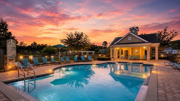 A swimming pool with lounge chairs, a covered seating area, and a sunset sky. - Family Escape Near Disney | Resort Amenities (Kissimmee)