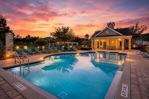 A swimming pool with lounge chairs, a covered seating area, and a sunset sky. - Family Escape Near Disney | Resort Amenities (Kissimmee)