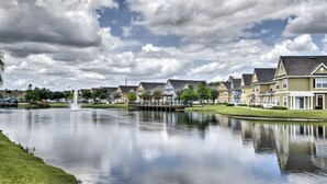 A row of houses along a calm lake with a fountain in the center. - Family Escape Near Disney | Resort Amenities (Kissimmee)