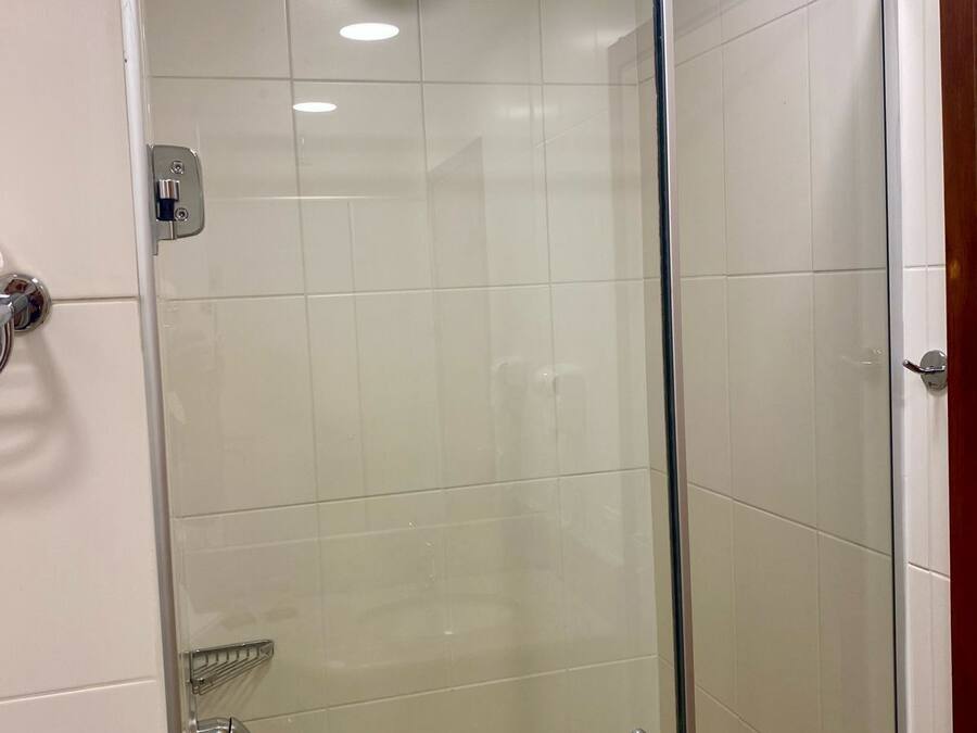 Cabina de ducha con paredes de vidrio, un cabezal de ducha de mano y puerta de vidrio.