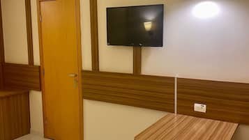 Habitación de hotel con puerta de madera, televisor de pantalla plana en la pared, una mesita de madera y una cama con manta color beige.