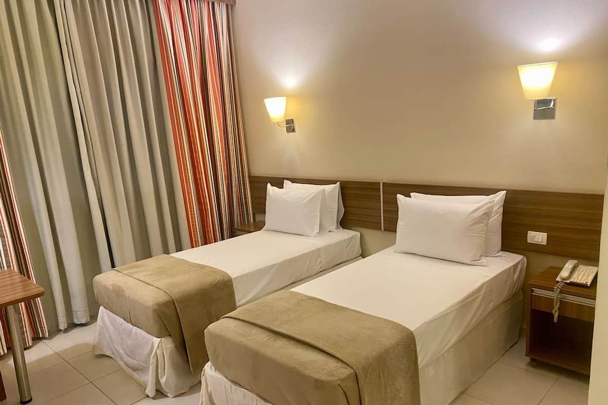 A hotel room with two beds, a small table, a telephone, and a curtain with a striped pattern.