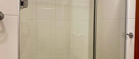 Cabina de ducha con paredes de vidrio, ducha de mano, toallero y un dispensador de papel higiénico a la vista.