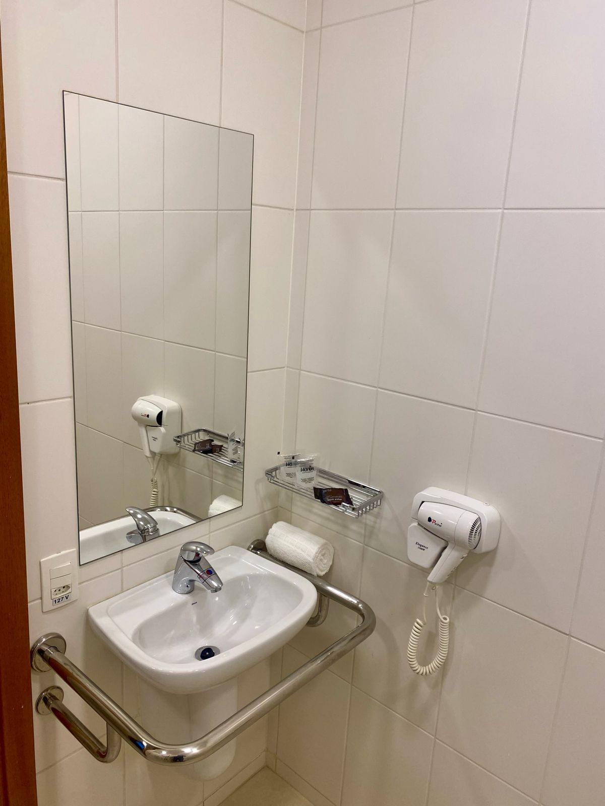 A bathroom with a white sink, a mirror, a hairdryer, and a towel dispenser.