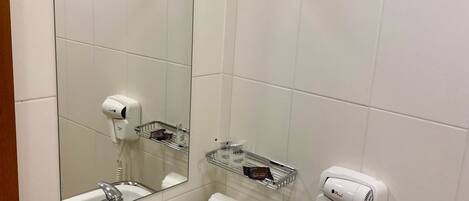 A bathroom with a white sink, a mirror, a hairdryer, and a towel dispenser.