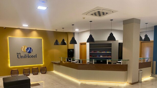 A hotel reception area with a modern design, featuring a reception desk, a digital display, and a seating area with stools.