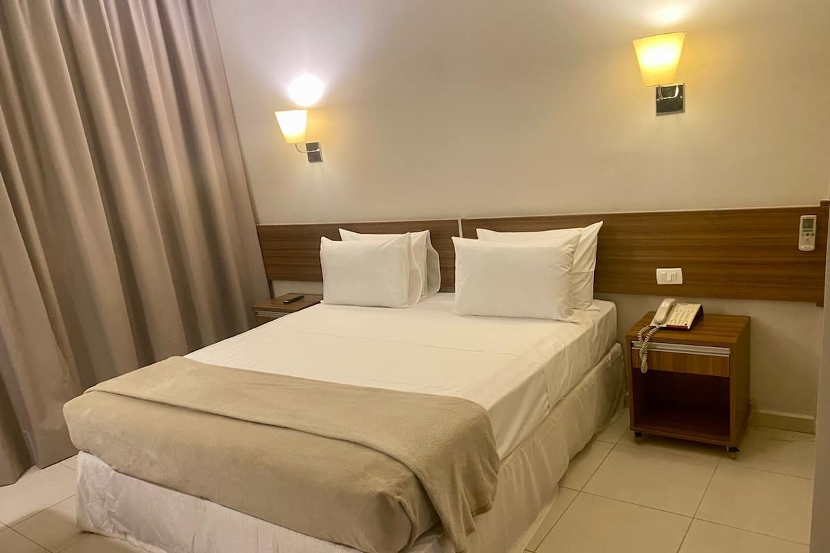 A hotel room with a large bed, two bedside tables, a bedside phone, and a wall-mounted light fixture.