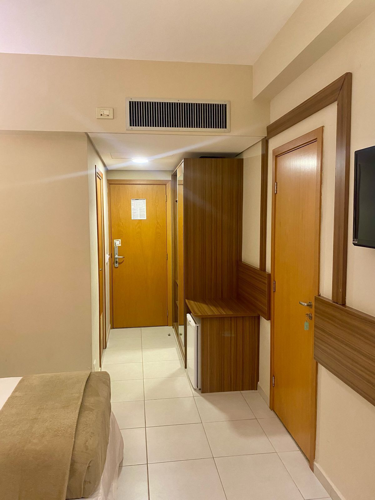 Pasillo de hotel con cama, armario de madera y puerta con espejo.