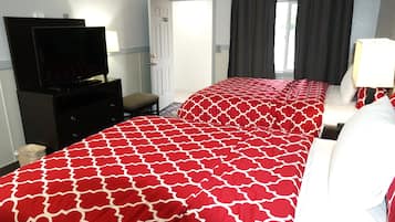 A hotel room with two beds, a TV, a desk, and a window with curtains.