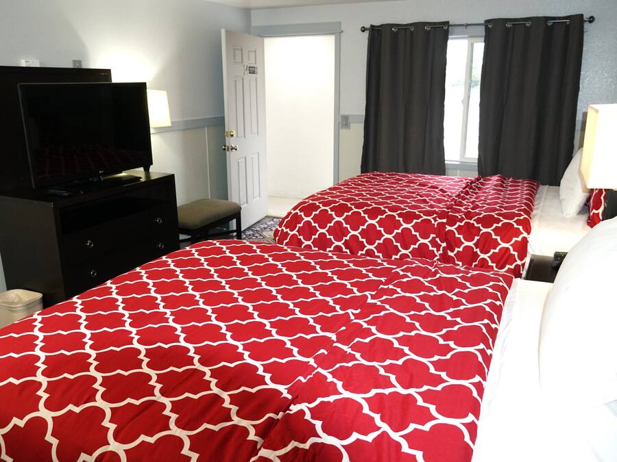A hotel room with two beds, a TV, a desk, and a window with curtains.