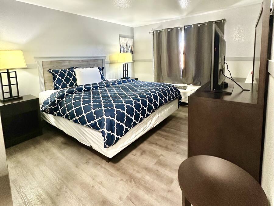 A hotel room with a bed, a desk, a chair, a TV, and a lamp.
