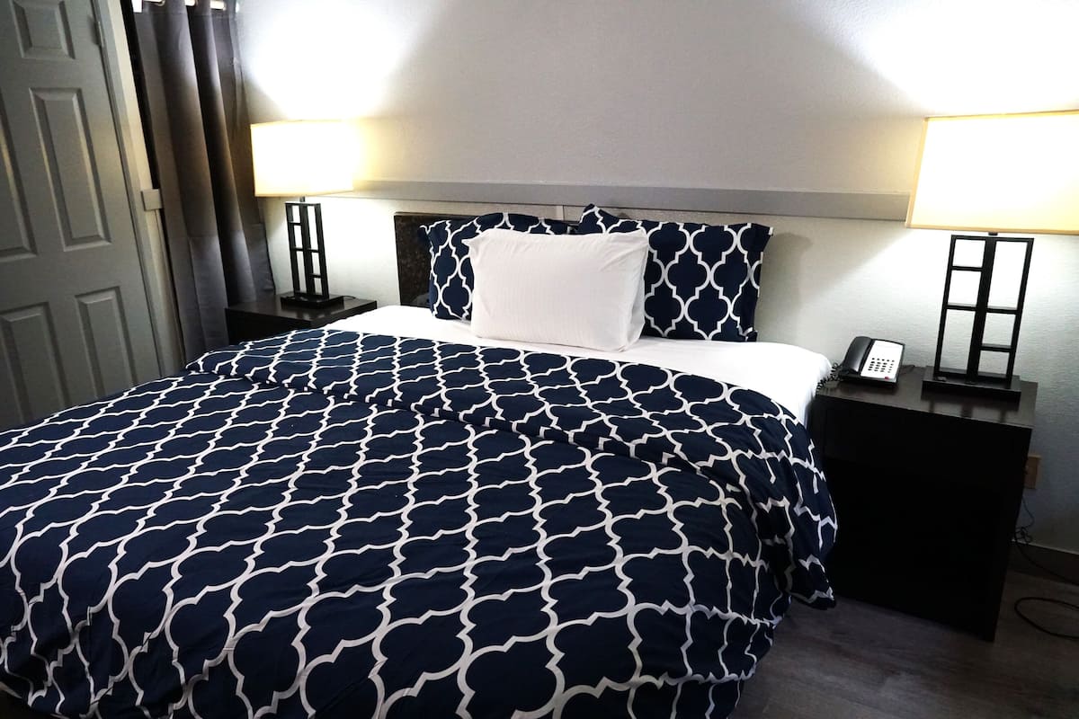 A neatly made bed with a patterned bedspread, a white pillow, and two bedside tables with lamps and a phone.
