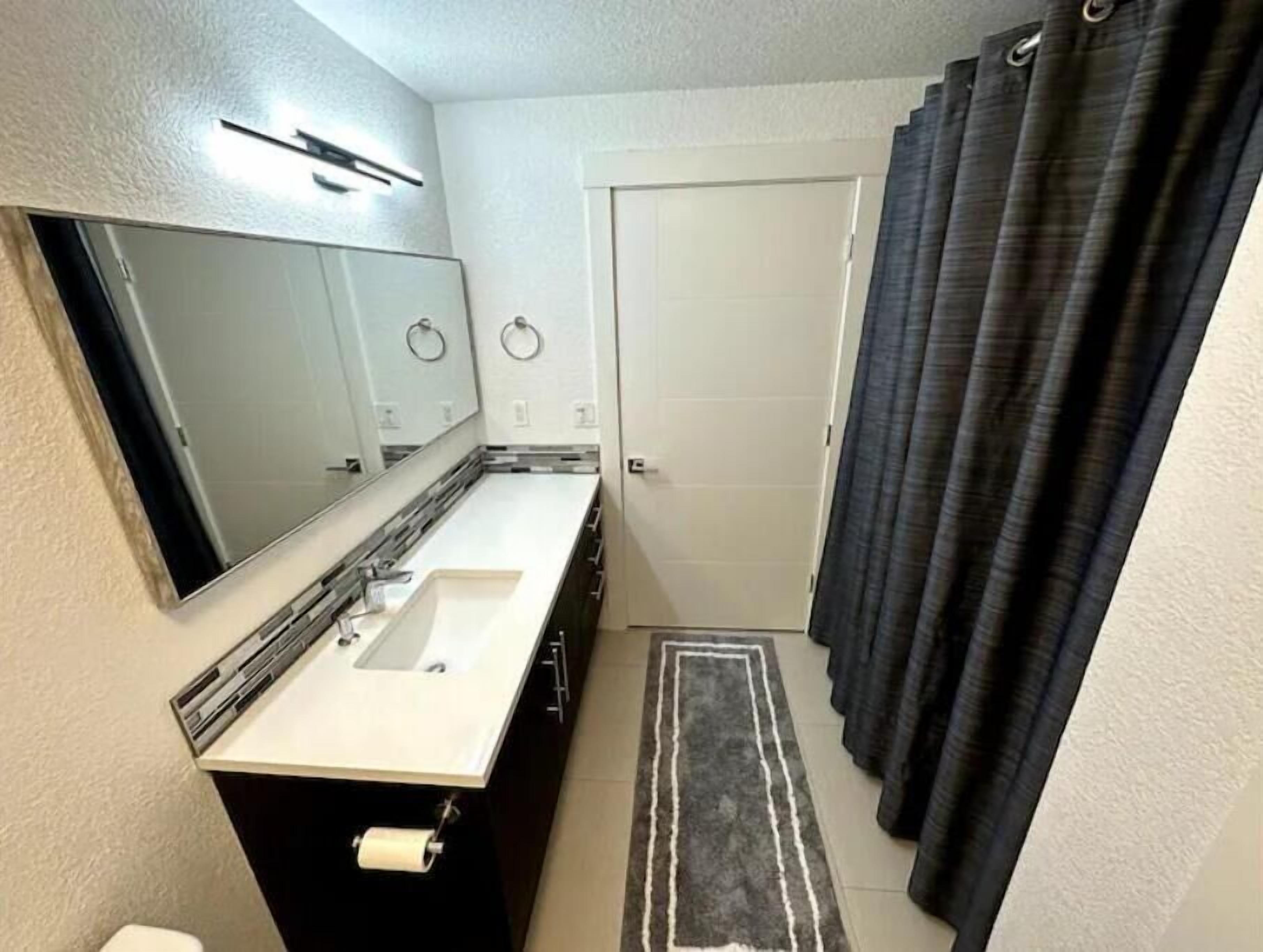 A bathroom with a double sink, a toilet, a mirror, a towel rack, and a shower curtain.