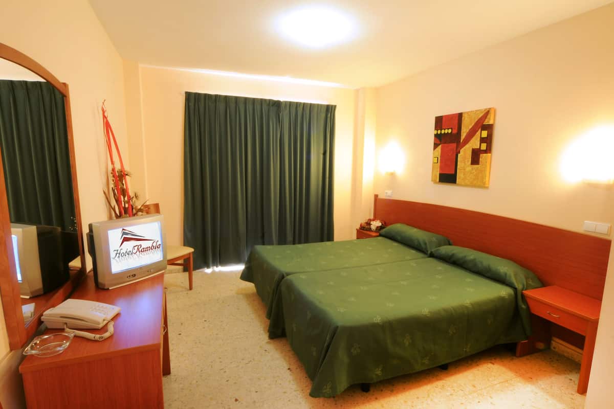 A hotel room with a bed, a desk with a TV, a telephone, and a nightstand.
