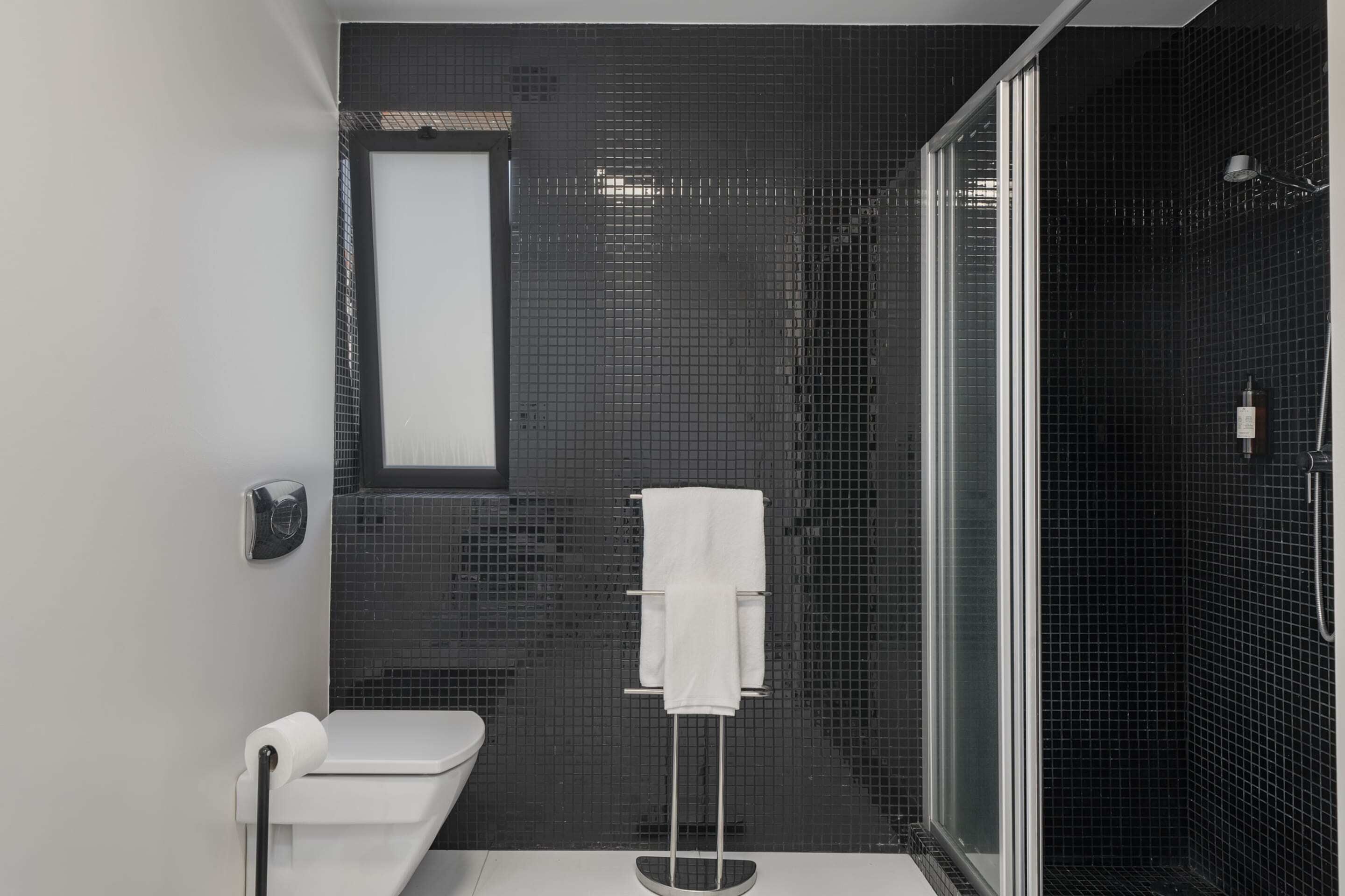 Une salle de bain moderne avec un mur recouvert de carreaux noirs, une douche en verre et des toilettes blanches.